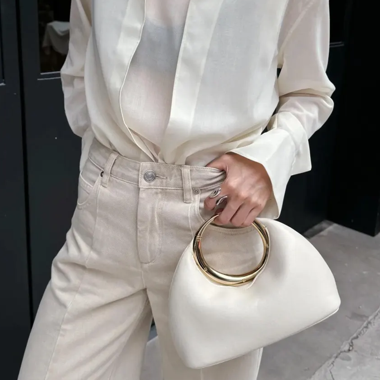 Soft Off-White Crescent Shaped Handheld Pouch With Polished Golden Circular Ring Grip, Central V-Cut Frame And Spacious Curved Open Inner Cavity