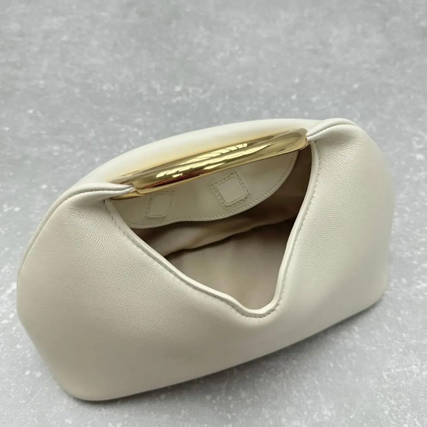 Soft Off-White Crescent Shaped Handheld Pouch With Polished Golden Circular Ring Grip, Central V-Cut Frame And Spacious Curved Open Inner Cavity